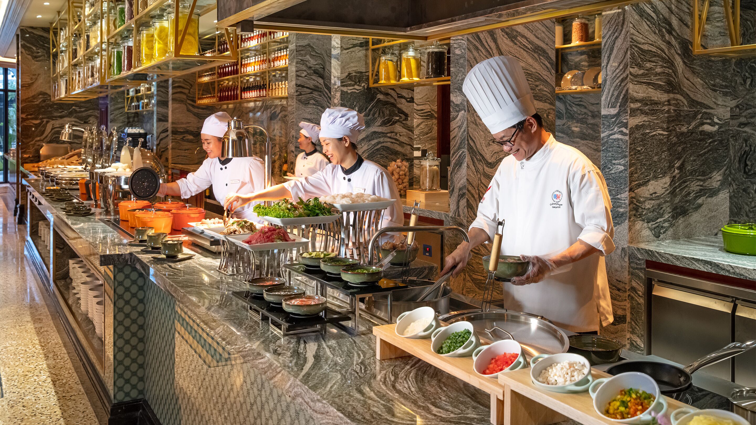 Una cocina profesional con chefs preparando alimentos, encimeras de mármol y diversos utensilios de cocina.