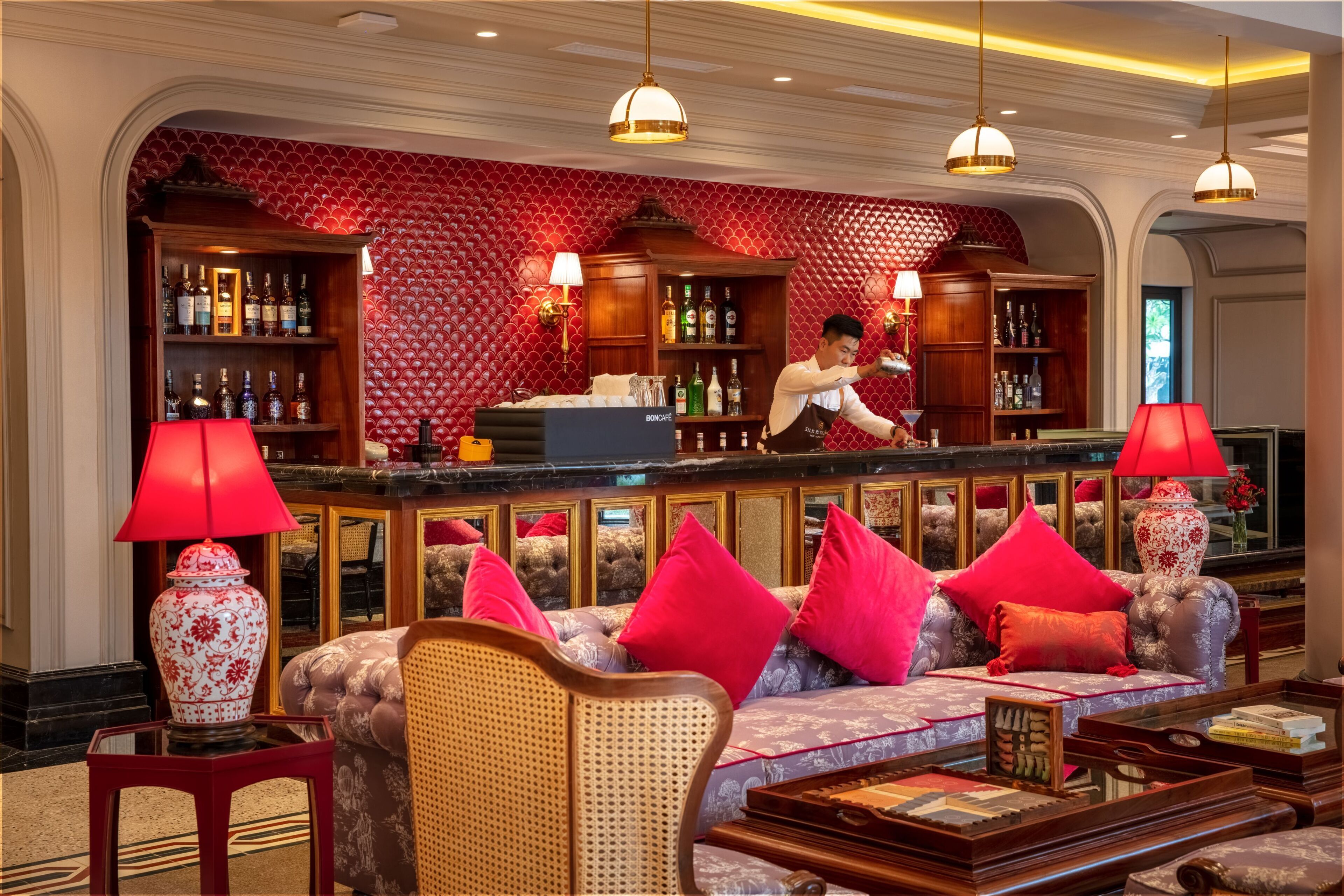 A bar area with a bartender, a sofa with red cushions, and a red patterned wall.