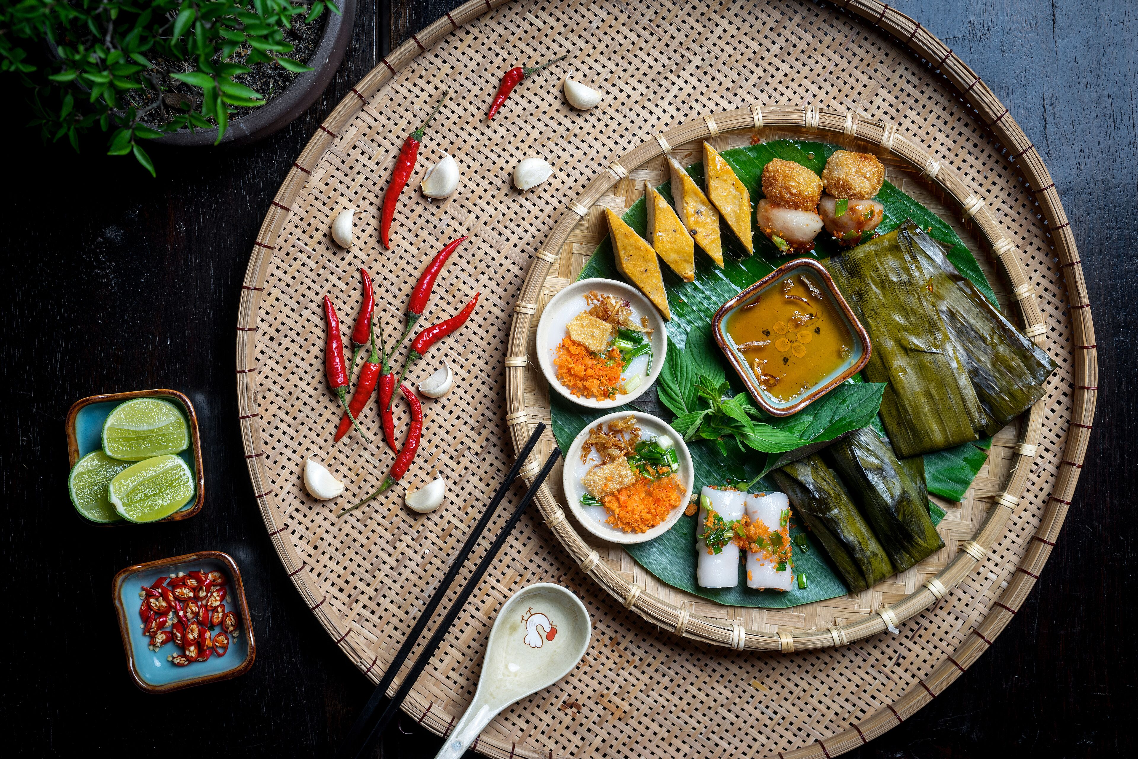 A traditional meal with various dishes on a woven mat, including rice cakes, dumplings, and a bowl of sauce.
