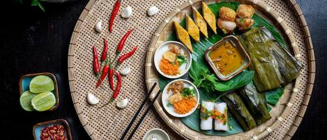 A traditional meal with various dishes on a woven mat, including rice cakes, dumplings, and a bowl of sauce.
