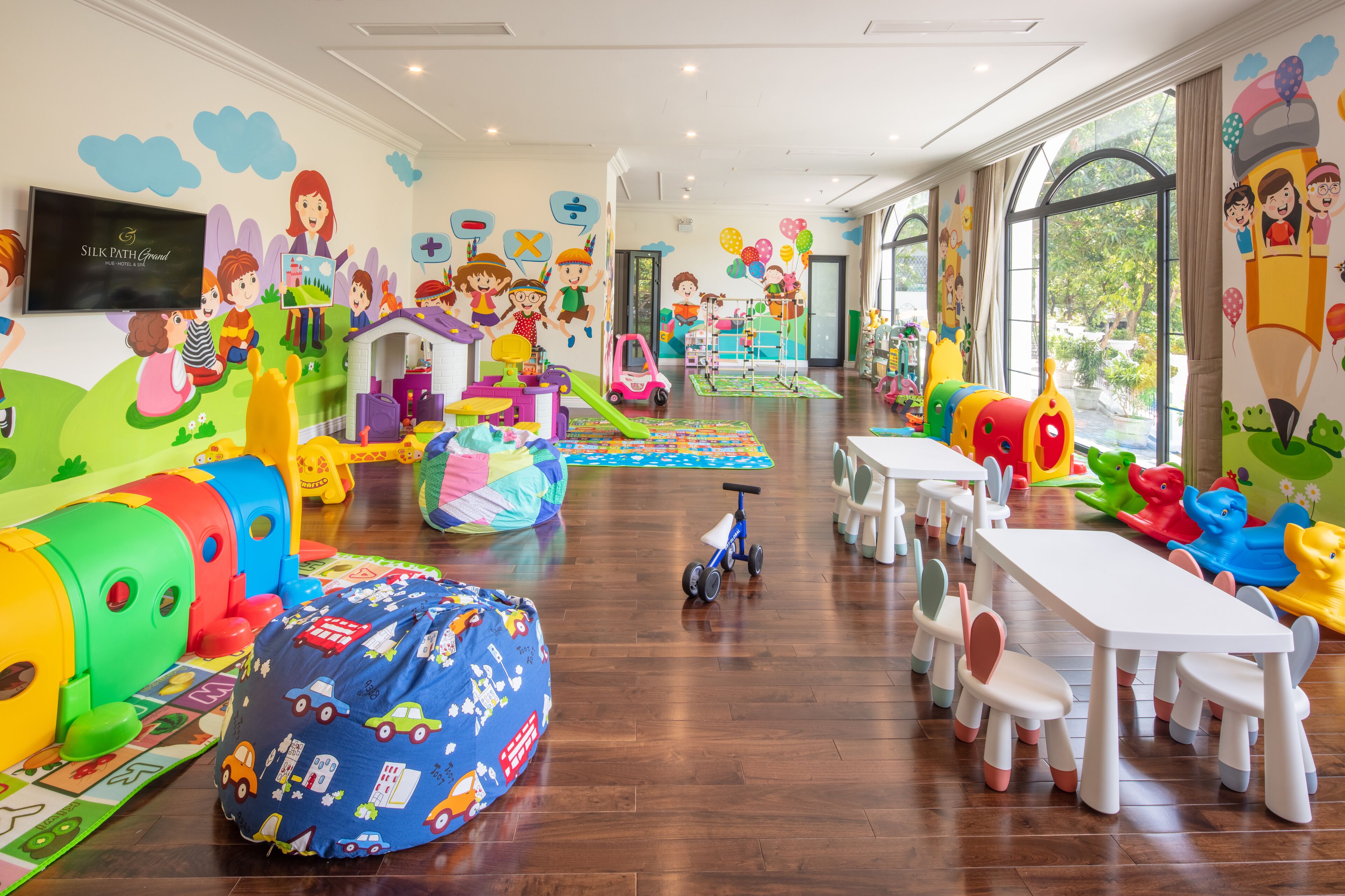 A children's playroom with colorful toys, a playhouse, and a large window providing natural light.