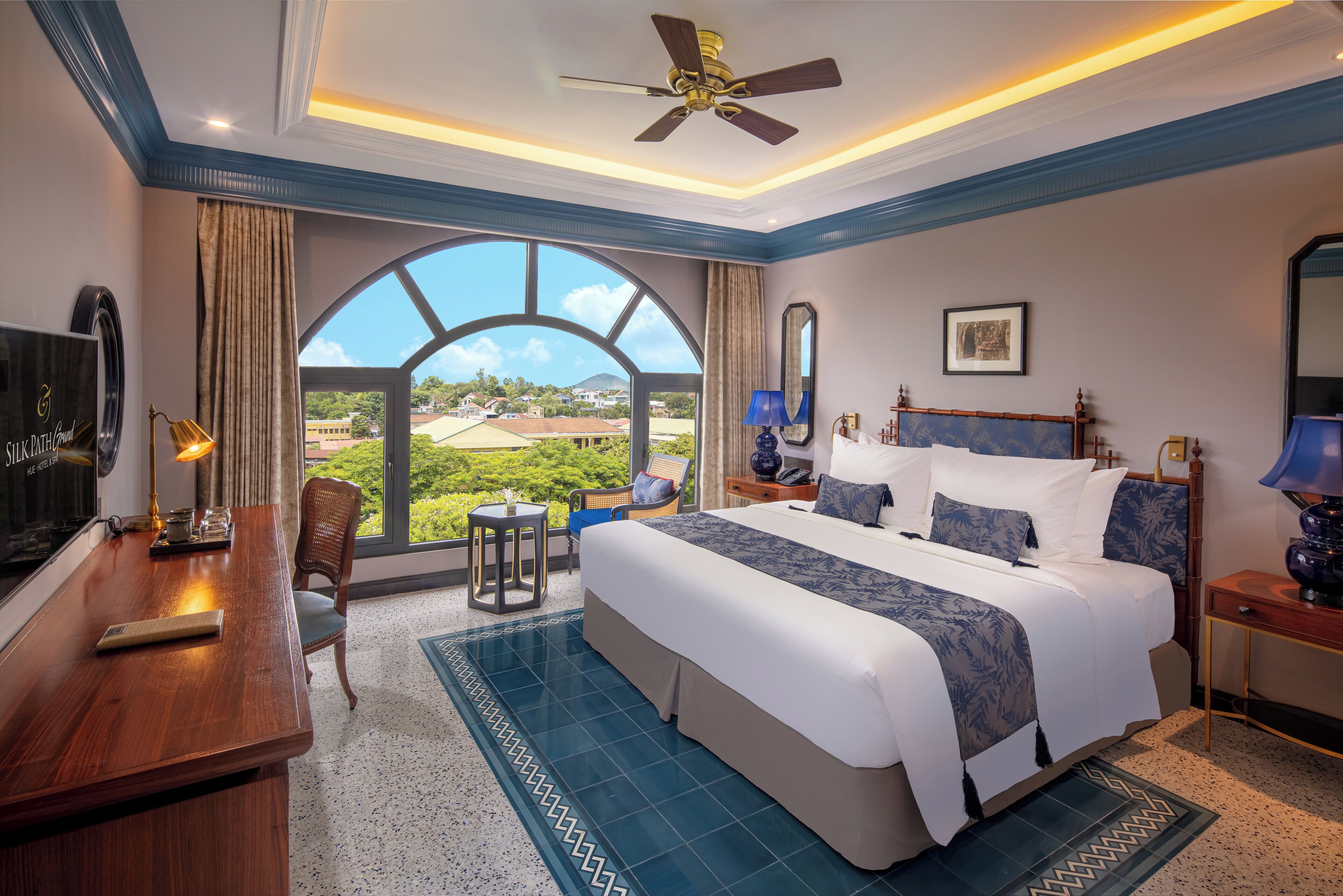 A hotel room with a large bed, a desk, a chair, a TV, and a view of the outdoors.
