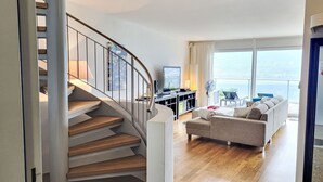 Una sala de estar moderna con una escalera curva, un sofá, un televisor y vistas al mar.