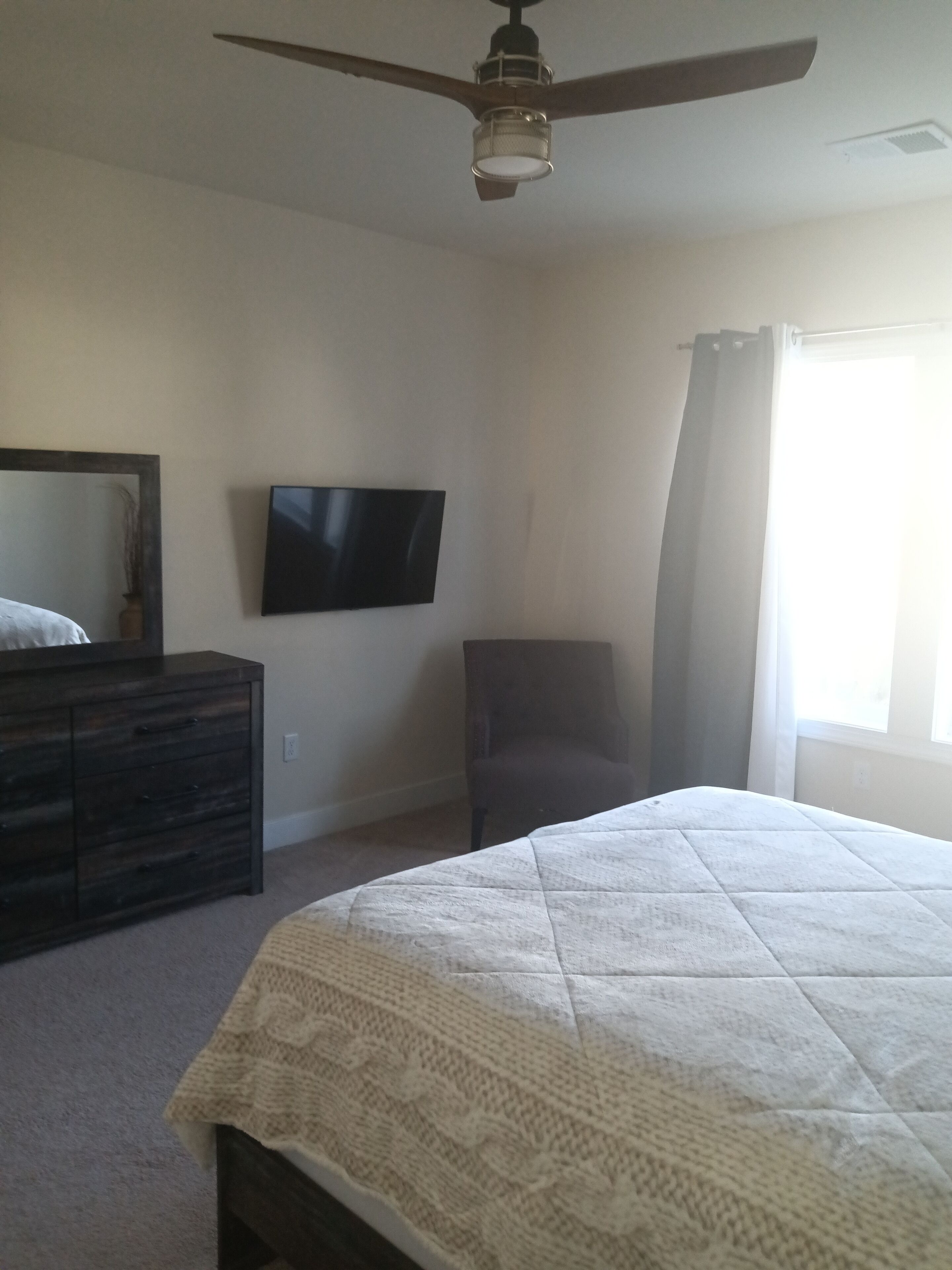 Une chambre à coucher comprenant un lit, une commode, une chaise, un téléviseur et un ventilateur de plafond.