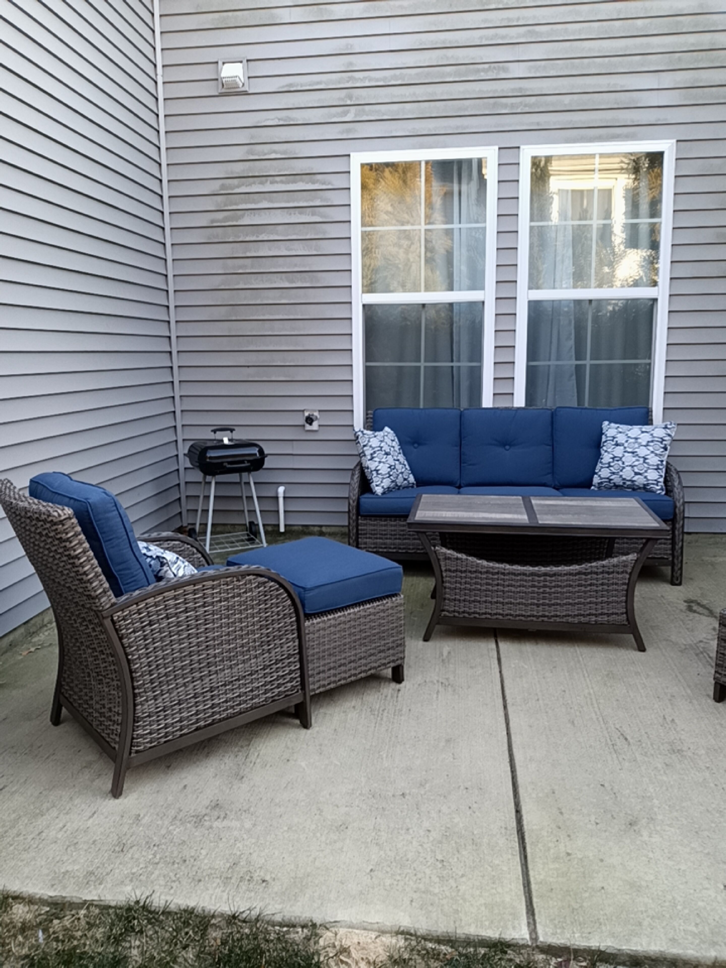 An outdoor patio with wicker furniture, a grill, and a window.