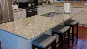 Une cuisine moderne avec des meubles blancs, un plan de travail en granit, des appareils électroménagers en acier inoxydable et un coin bar avec des tabourets.