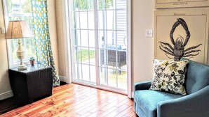 Un salon doté d’un parquet en bois, d’un canapé bleu, d’un coussin à motifs, d’une lampe et d’une fenêtre ornée de rideaux à motifs.