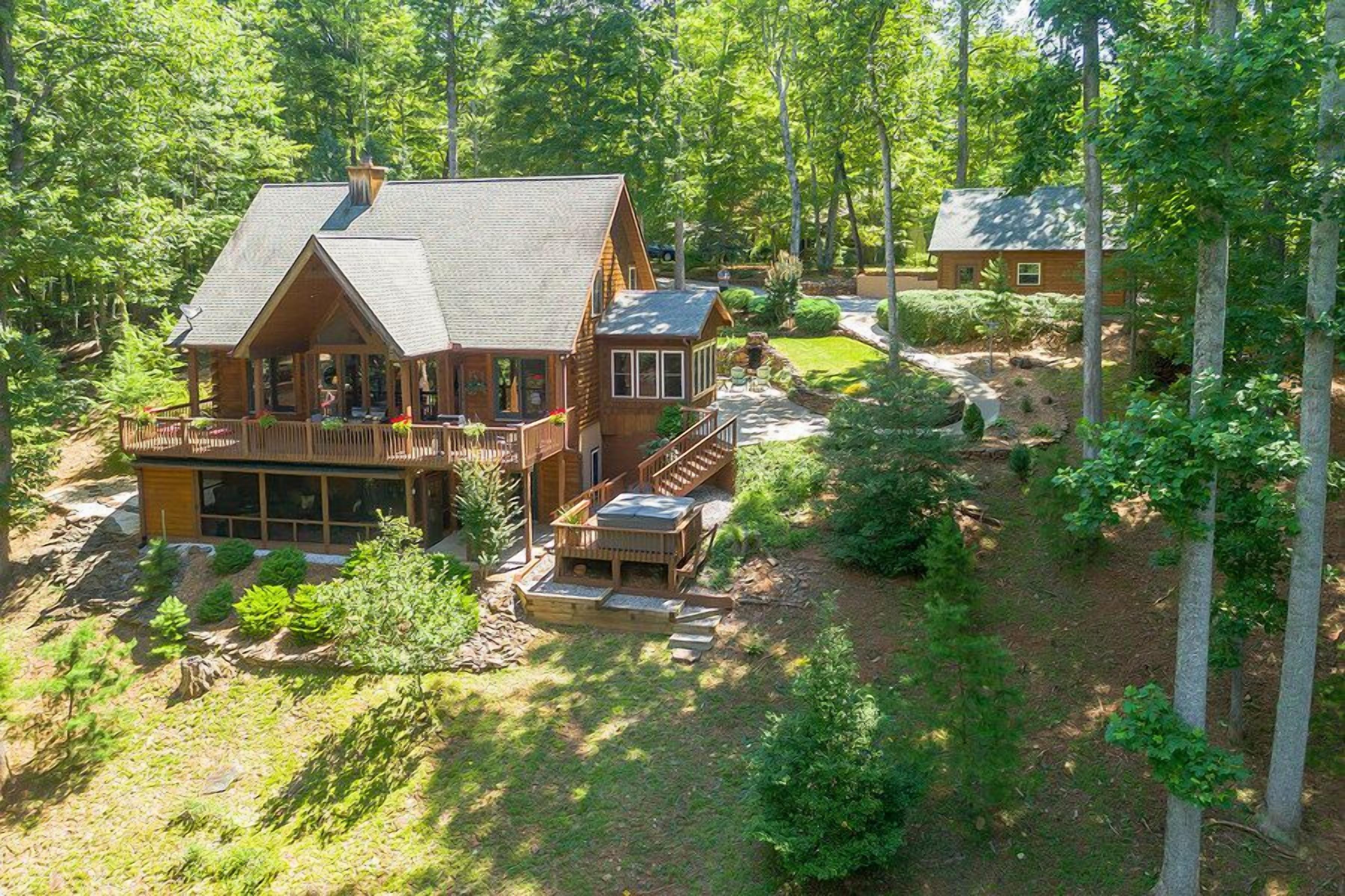 A large wooden cabin with a porch and deck, surrounded by dense forest.