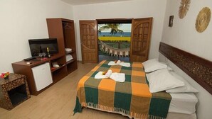 Habitación de hotel con cama, escritorio con televisor, minibar y vista a la playa a través de una puerta.