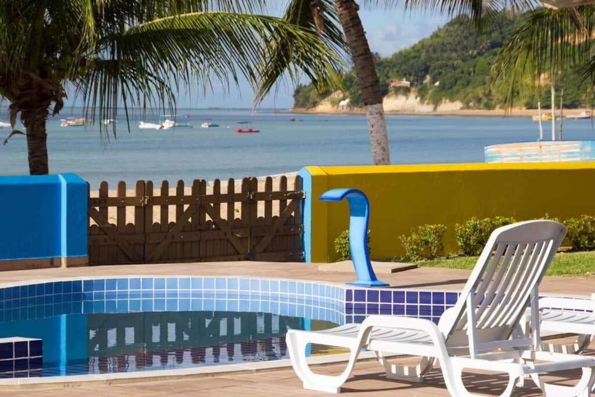 A pool area with tiled flooring, a wooden fence, and two white lounge chairs.