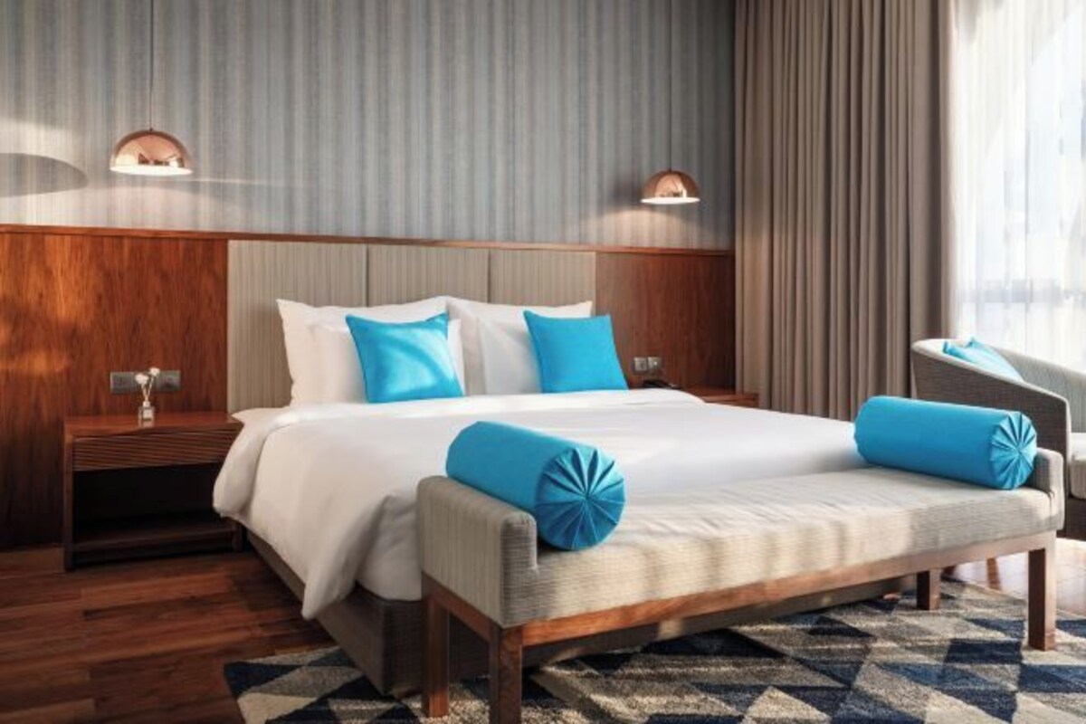 Una habitación de hotel con una cama grande, dos mesitas de noche, un sofá y una ventana con cortinas.