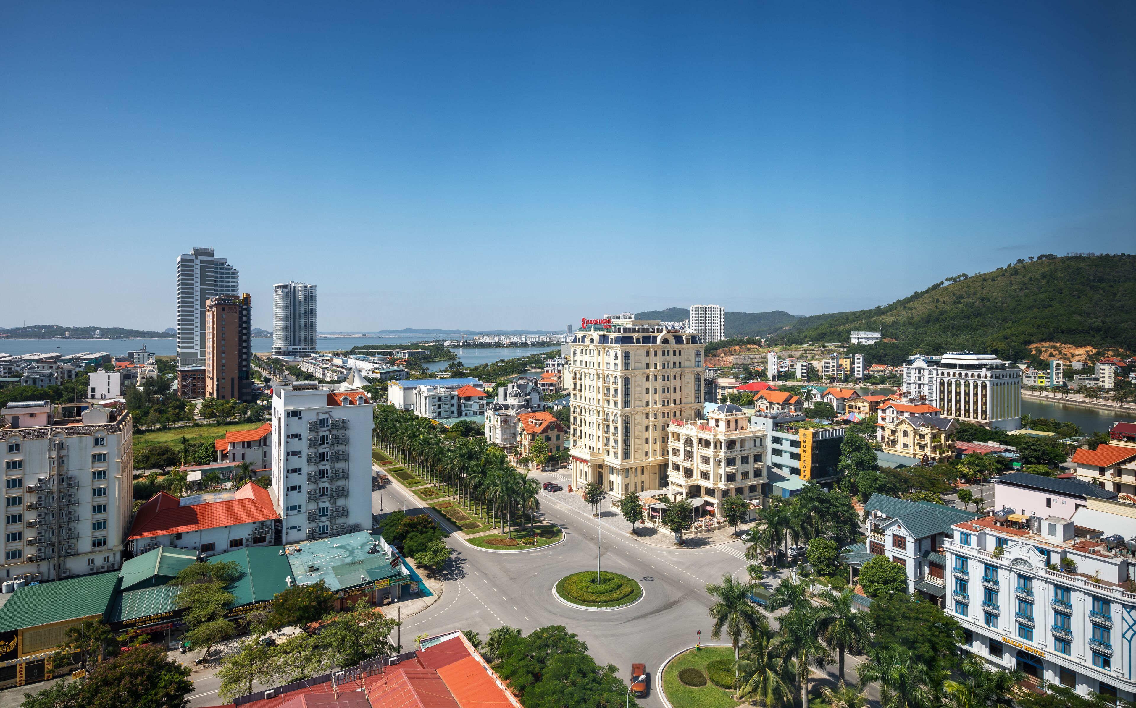 A cityscape with a mix of modern and historic buildings, a central roundabout, and a body of water in the background.