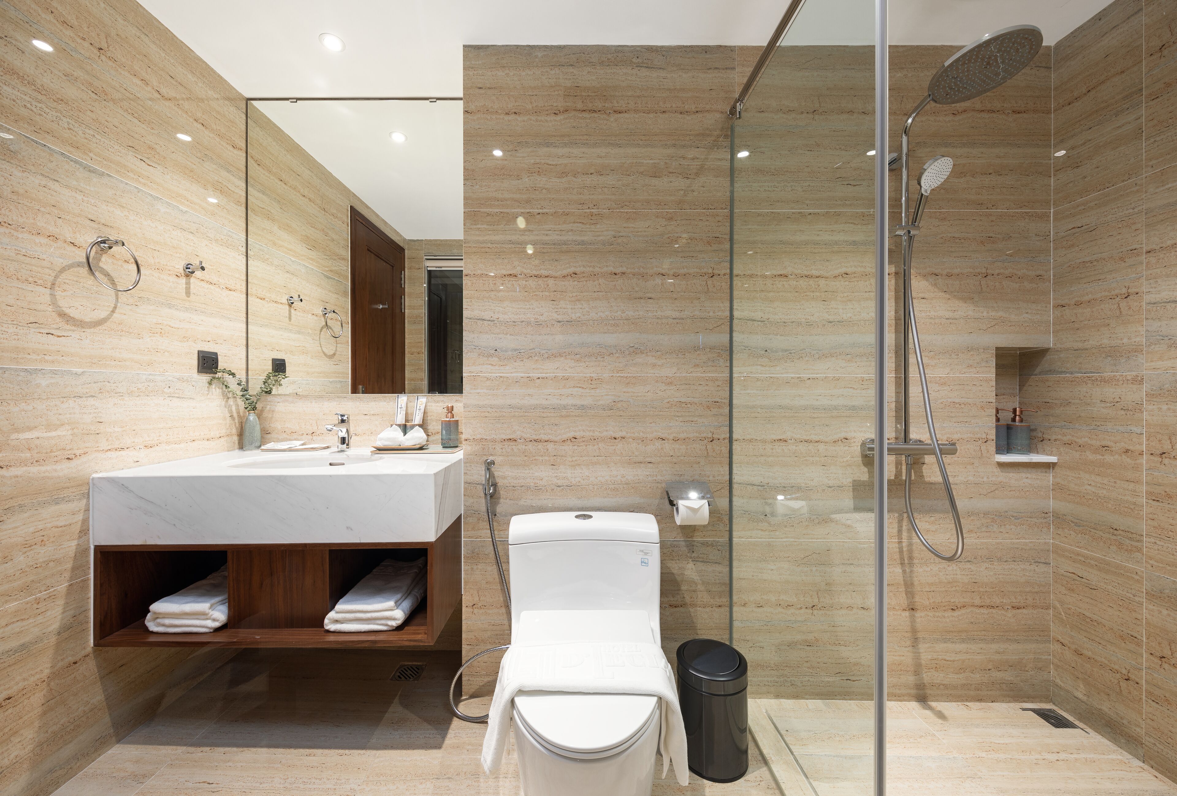 A modern bathroom with a glass-enclosed shower, a wooden vanity, and a marble-tiled wall.
