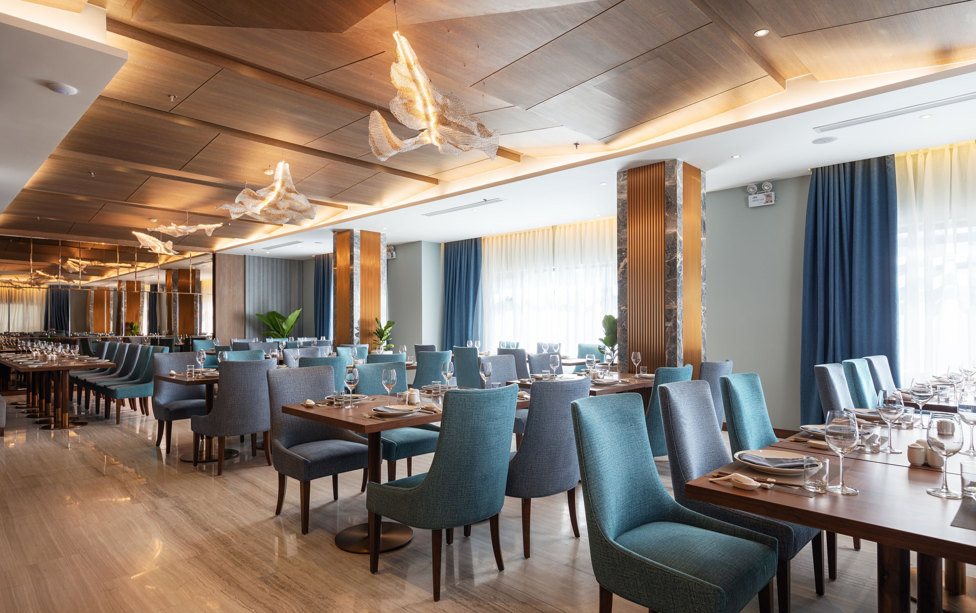 Un comedor amplio con techos altos, modernos candelabros y una larga mesa dispuesta para una comida.