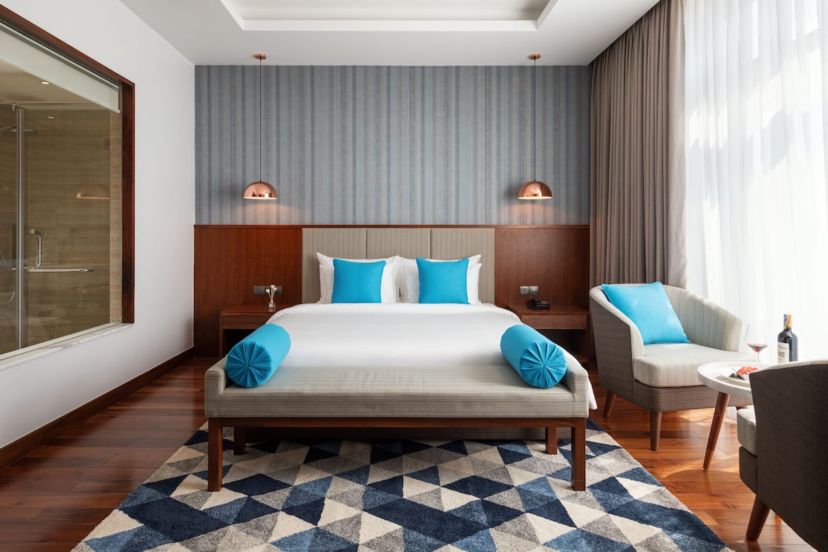 A hotel room with a large bed, two nightstands, a chair, a small table, and a large window.