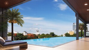 Un área de piscina moderna con sillas de descanso, cielo azul despejado y vista a edificios de la ciudad.