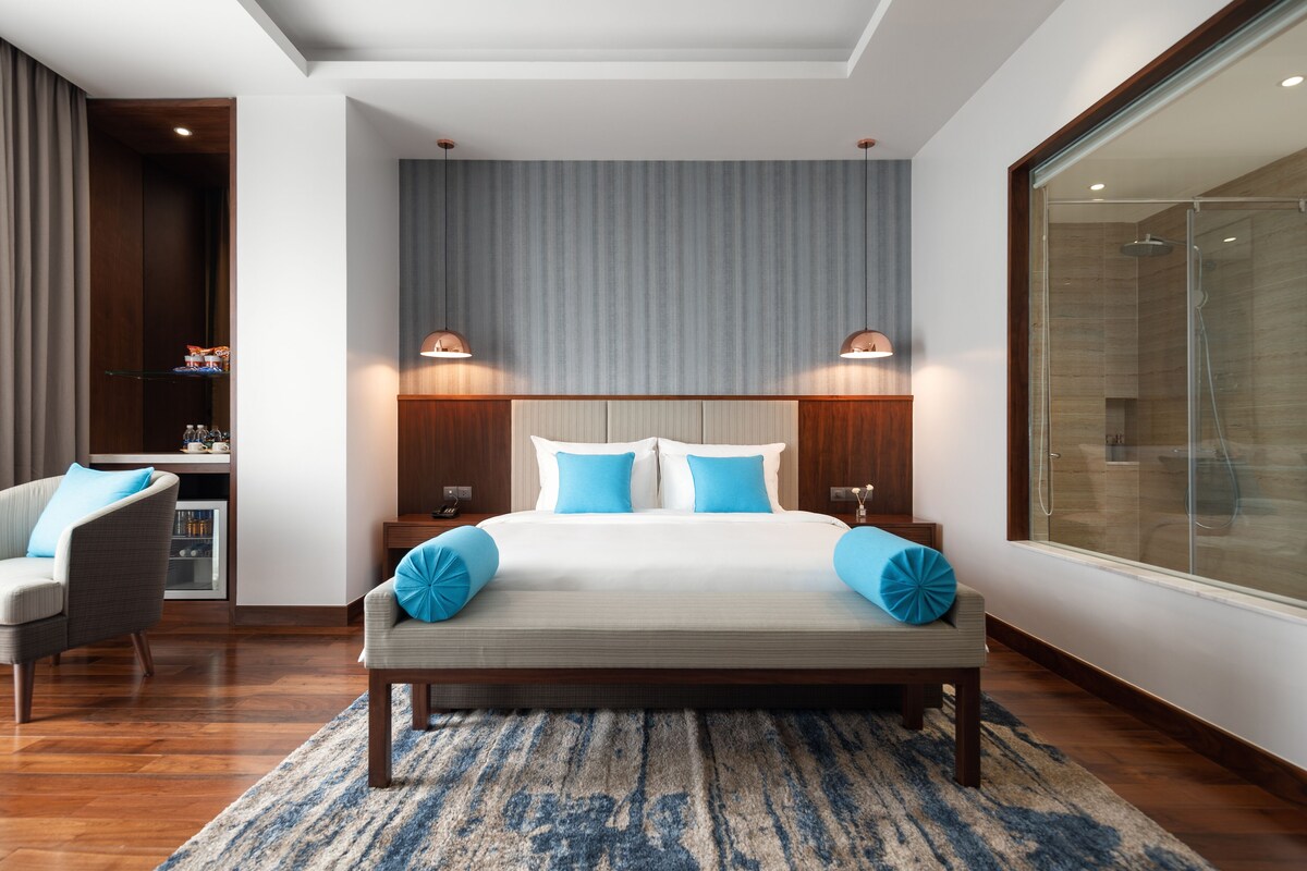 A modern bedroom with a large bed, two bedside tables, a nightstand, a chair, and a large window.
