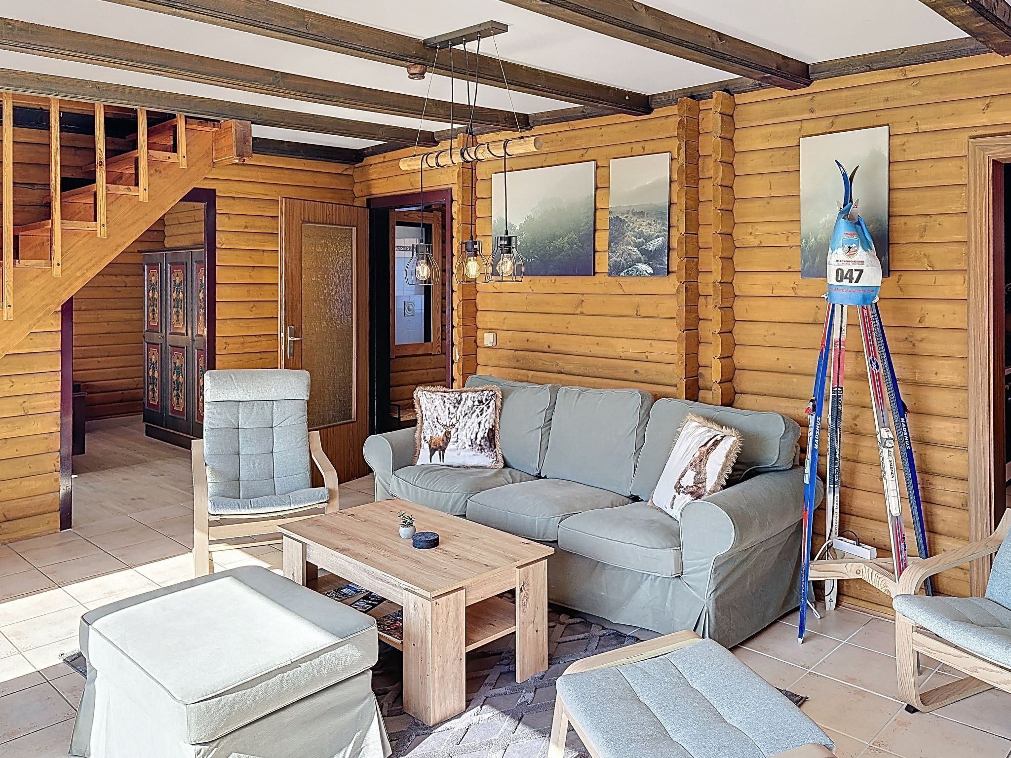 A log cabin interior with a staircase, a grey sofa, a wooden coffee table, and a ski pole rack.