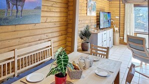A wooden cabin interior with a dining table, chairs, a clock, a television, and a painting of a cow. - Franzi 2 by Interhome (Arrach)