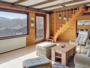 A log cabin interior with a wooden staircase, a large window with a view of a forest, and a cozy seating area with a table and chairs. - Franzi 2 by Interhome (Arrach)