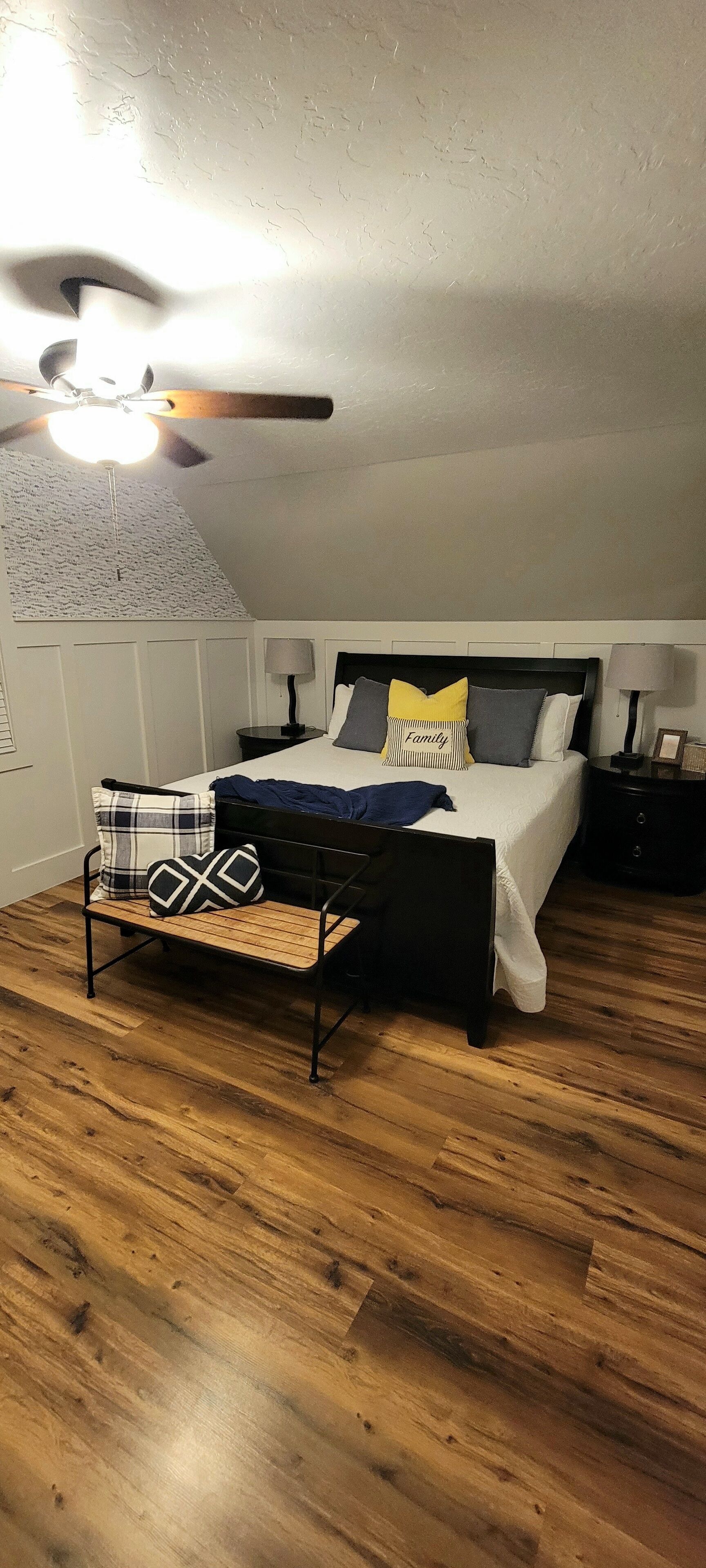 Une chambre à coucher avec un lit, des tables de chevet, un ventilateur de plafond et un plancher en bois.