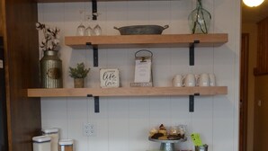 A kitchen with wooden shelves holding various items like a vase, a metal container, and a sign that says "create a life you love."