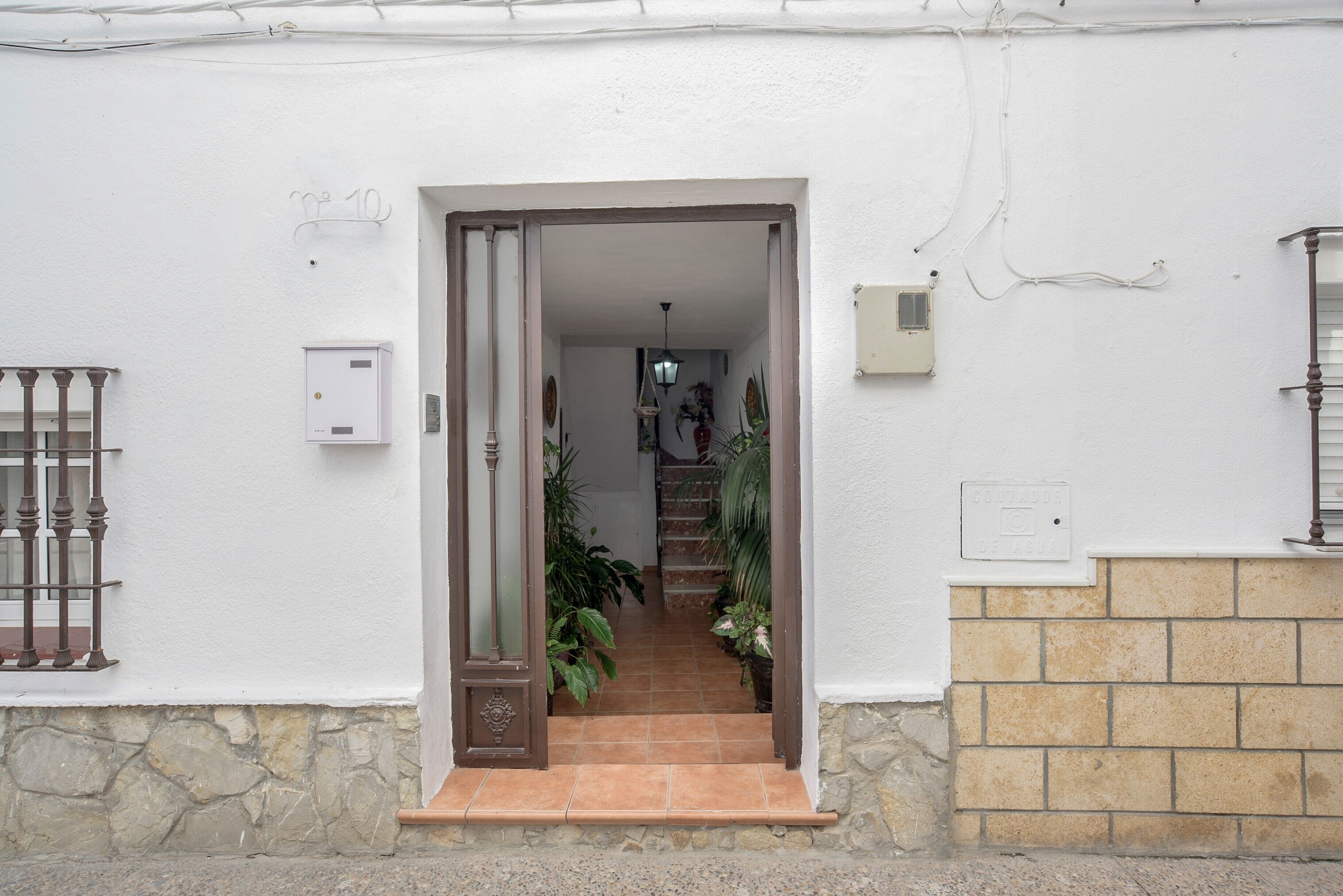 Un bâtiment blanc avec un socle en pierre, une porte en bois et un escalier carrelé menant à un étage supérieur.