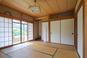 A traditional Japanese room with tatami flooring, sliding doors, and a view of greenery outside.