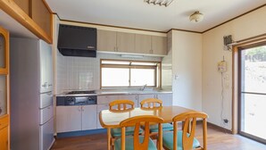 A kitchen with wooden cabinets, a stainless steel refrigerator, a built-in oven, and a dining table with chairs. - Sasayakana Ouchi Fuuki (Futtsu)