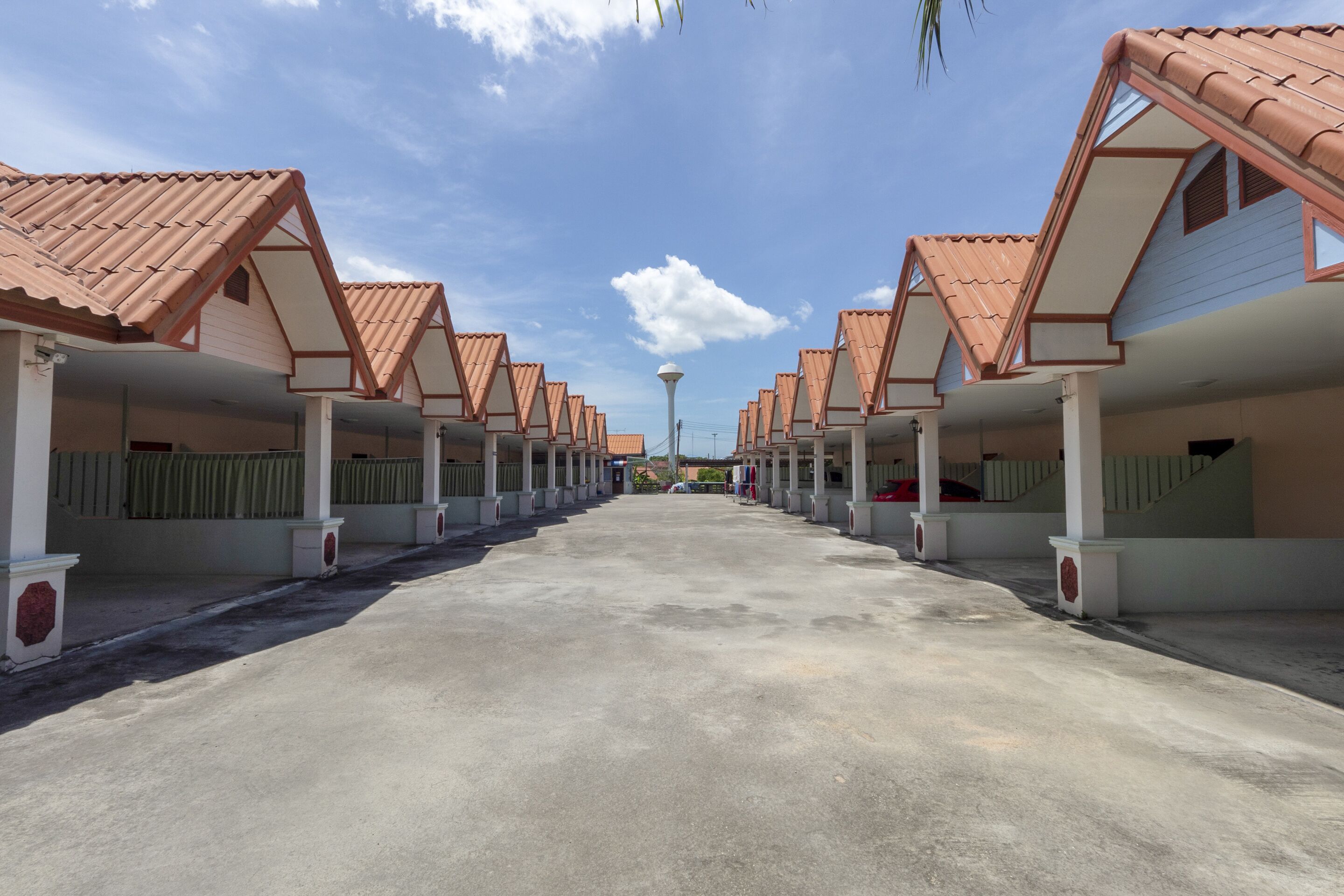 A row of hotel rooms with red-tiled roofs and white walls, a central walkway, and a street lamp in the distance.