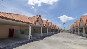 A row of motel-style buildings with uniform red-tiled roofs and white pillars, a clear sky, and a distant lamp post. - OYO 1070 Paradise Resort (Ban Chang)
