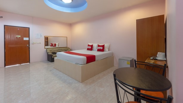 A hotel room with a bed, a desk, a chair, a small table, a mirror, a door, and a ceiling light fixture. - OYO 1070 Paradise Resort (Ban Chang)