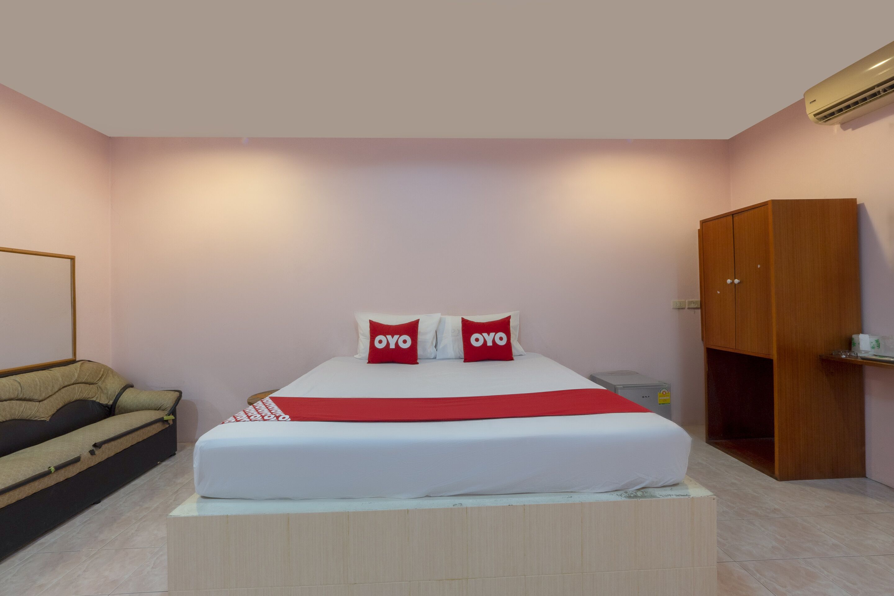 Une chambre à coucher comprenant un lit, une armoire en bois, un canapé et un appareil de climatisation.