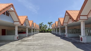 A row of motel rooms with a central concrete walkway, numbered columns, and a clear sky. - OYO 1070 Paradise Resort (Ban Chang)