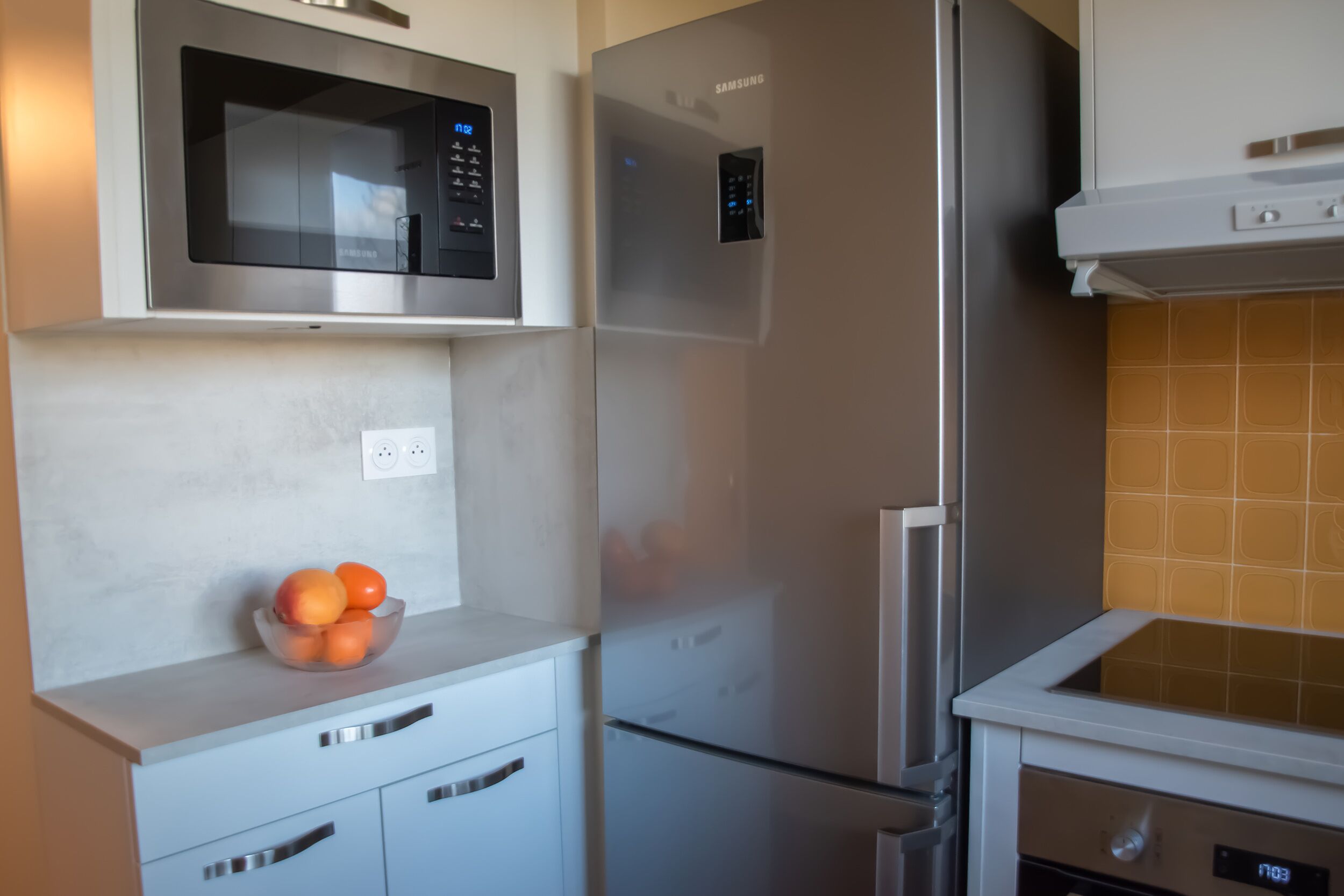 A kitchen with a microwave, refrigerator, and a bowl of fruit on the counter.