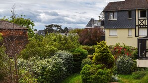 Ein Wohngebiet mit einem gepflegten Garten, einem Haus mit dunklem Dach und einem Gebäude mit weißer Fassade und schwarzer Verzierung.
