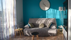 Ein modernes Wohnzimmer mit einem grauen Sofa, gemusterten Kissen, einer runden Wanduhr, einem kleinen runden Tisch und einer hohen Stehlampe.