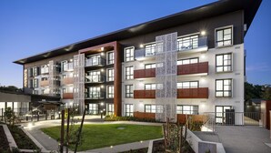 Un edificio residencial de varios pisos con balcones, una entrada bien iluminada y un patio ajardinado.