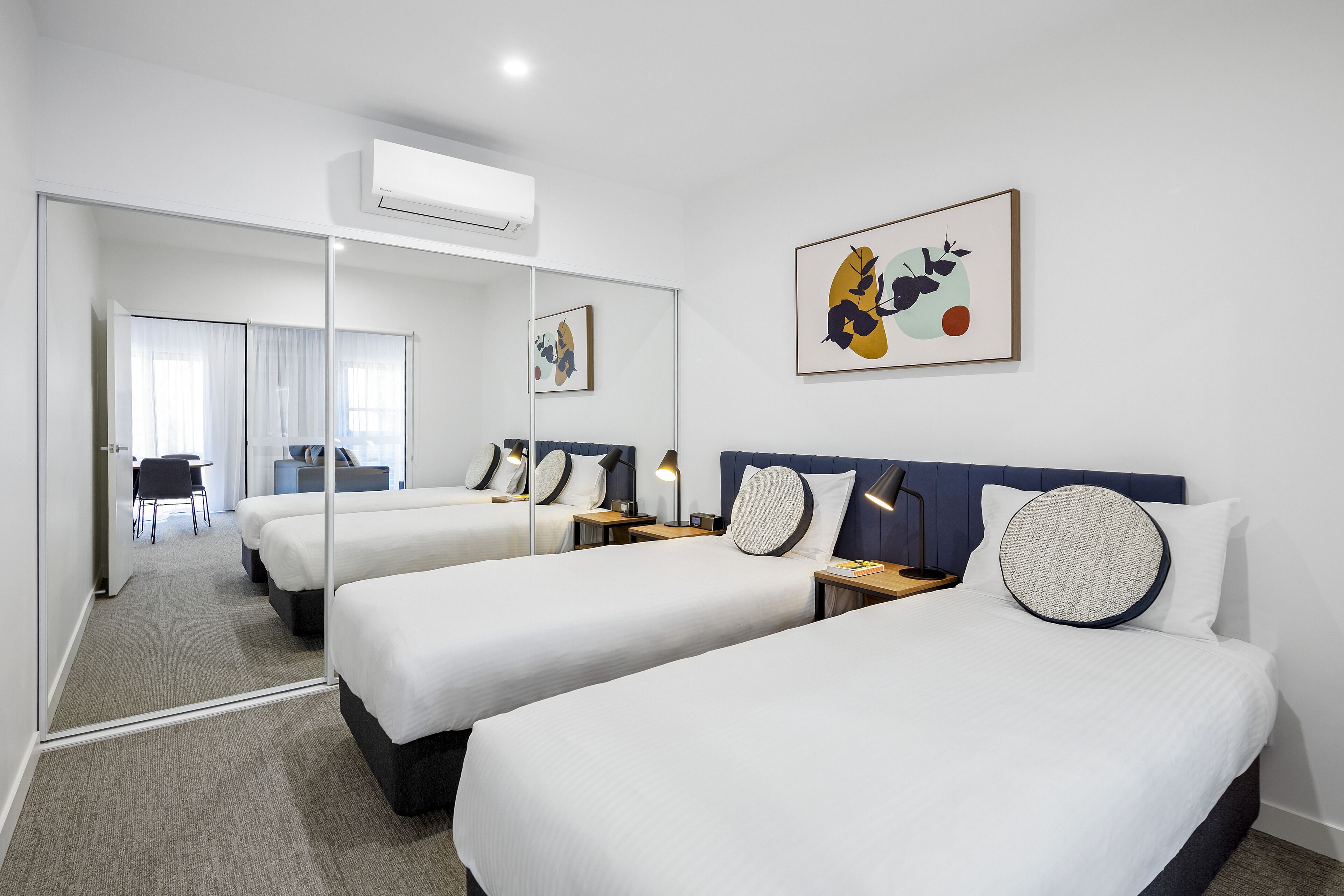 A hotel room with two beds, a large mirror, and artwork on the wall.