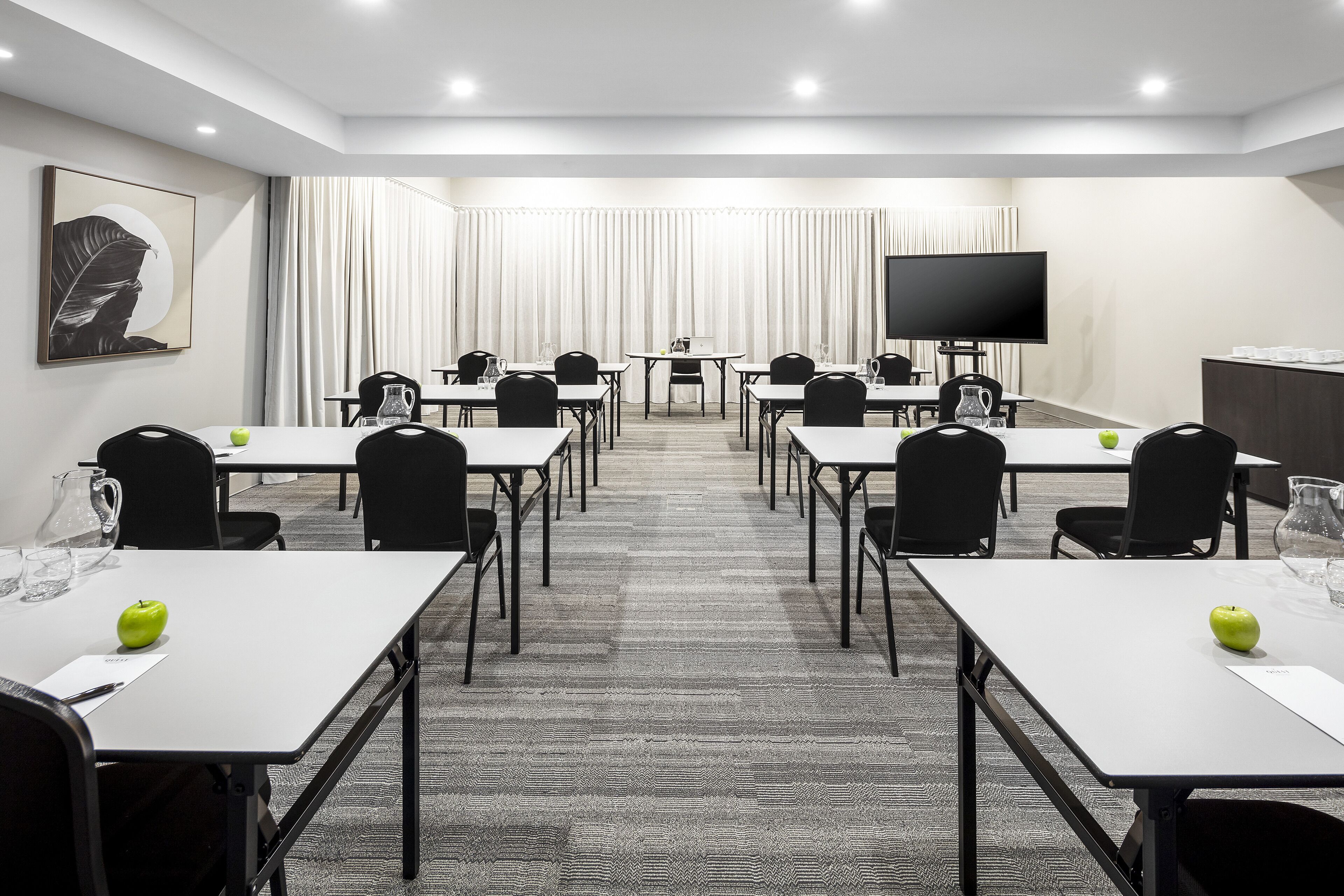 A conference room with multiple tables and chairs, a flat-screen TV, and a large window with curtains.