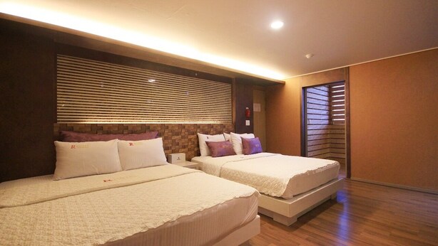 Habitación de hotel con dos camas, una pared de ladrillo decorativa y una ventana con persianas.