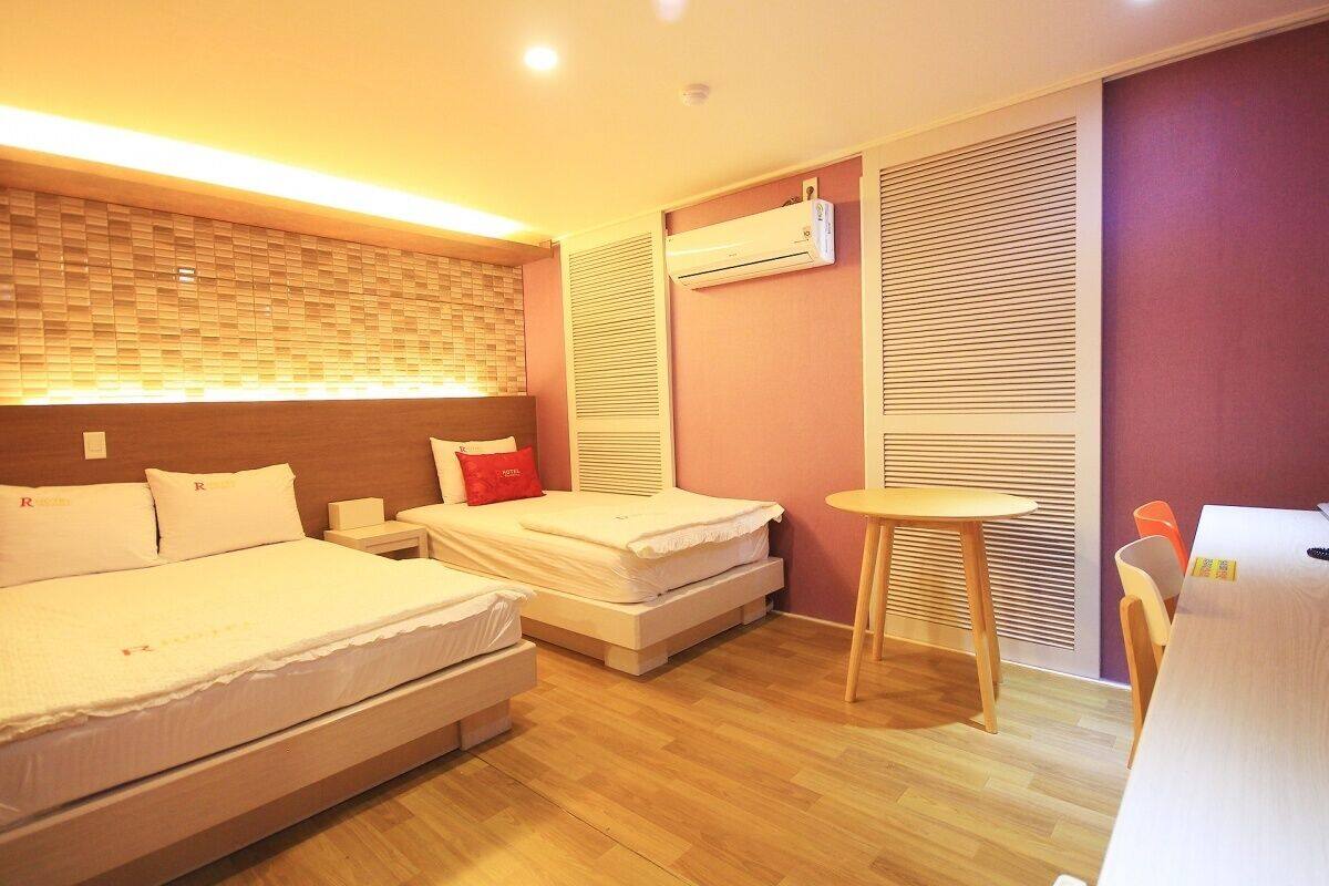 A hotel room with two beds, a small table, and an air conditioning unit.