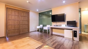 Habitación moderna con un armario de madera, un escritorio con computadora, televisor de pantalla plana y un refrigerador pequeño.