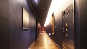 Un pasillo largo y estrecho con paredes oscuras y suelo pulido, que conduce a una puerta con cerradura electrónica.