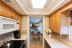 Una cocina con armarios de madera, microondas, estufa y comedor con mesa y sillas.