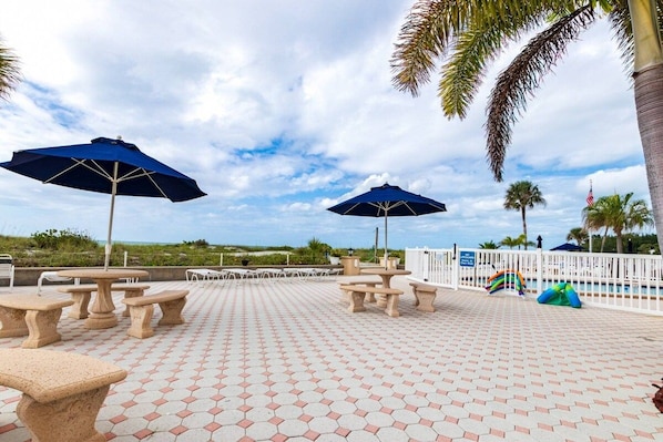 Un espace aménagé au bord de la piscine, avec des carreaux hexagonaux, des tables d’extérieur et des parasols.