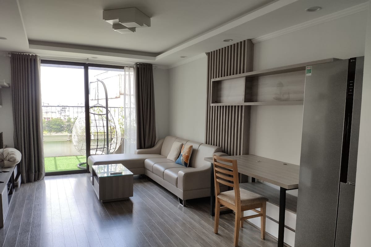 A modern living room with a sofa, a wooden chair, a glass coffee table, and a built-in wooden shelf.