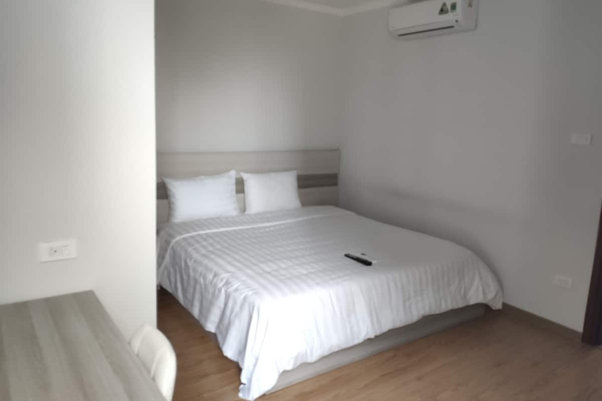 A bedroom with a bed, a bedside table, and an air conditioning unit on the wall.