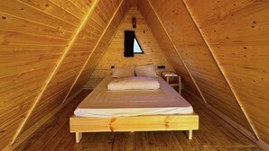 Ein rechteckiger Raum mit Holzwänden, einem Bett, einem kleinen Tisch und einem Fenster.