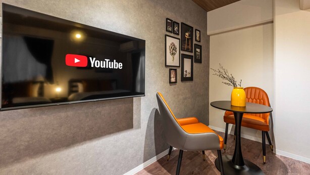 A modern room with a YouTube logo on the wall, a round table with a yellow vase, and two chairs with orange and gray upholstery. - Bird Land in Shinsaibashi east (Osaka)